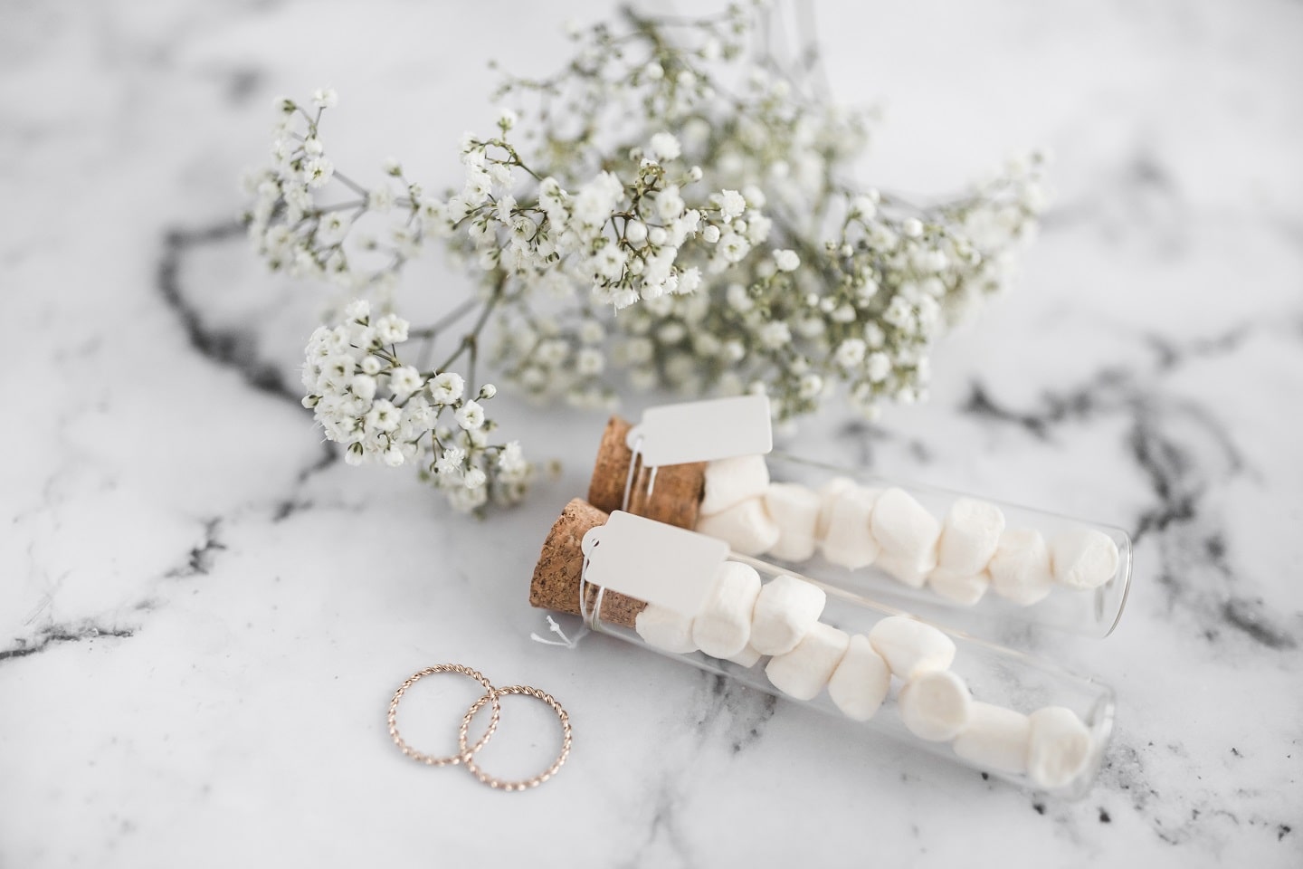 wedding-rings-marshmallow-test-tubes-with-tag-baby-s-breath-flowers-white-textured-background-min.jpg